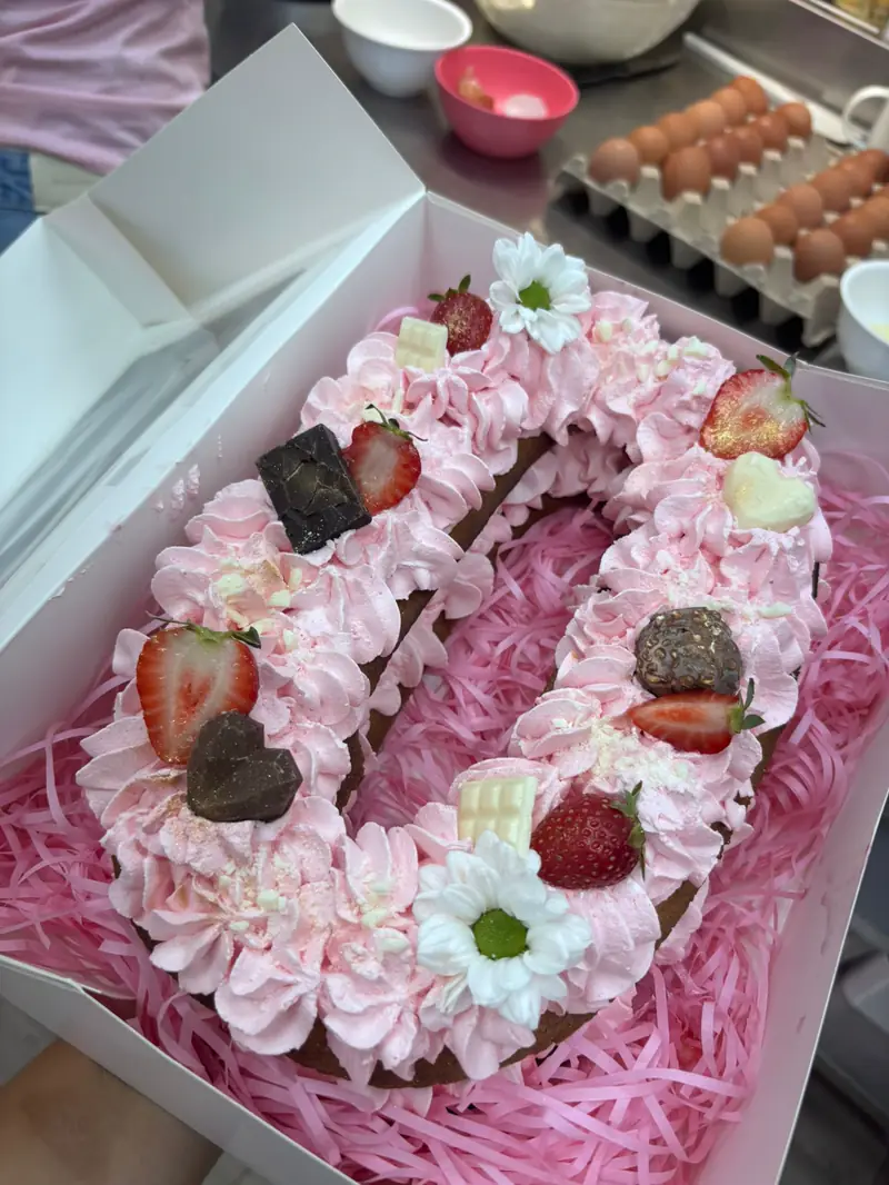 Tarta con forma de número ocho decorada con crema rosa, fresas y flores
