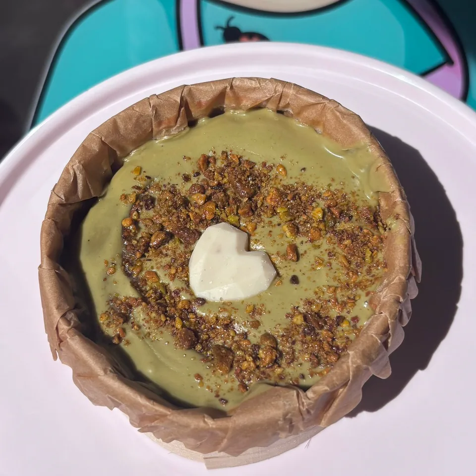 Cheesecake artesanal de pistacho decorada con frutos secos y un corazón de chocolate blanco